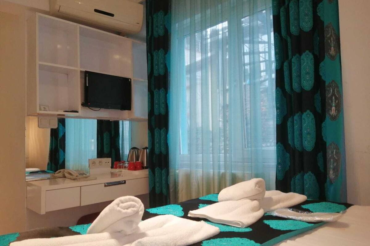 A hotel room with a bed, a TV mounted on the wall, a desk with a phone, and a window with curtains.