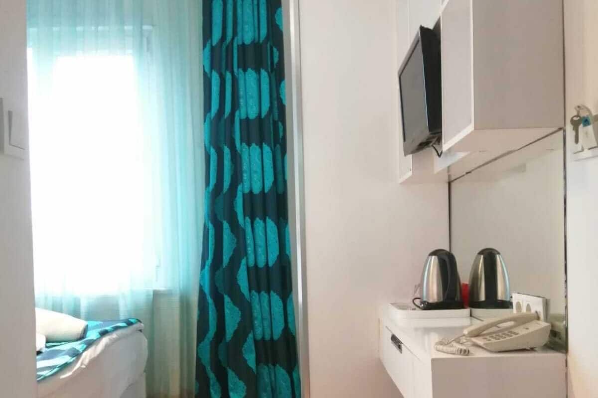 A compact hotel room with a bed, a small kitchenette, a TV, and a window with curtains.