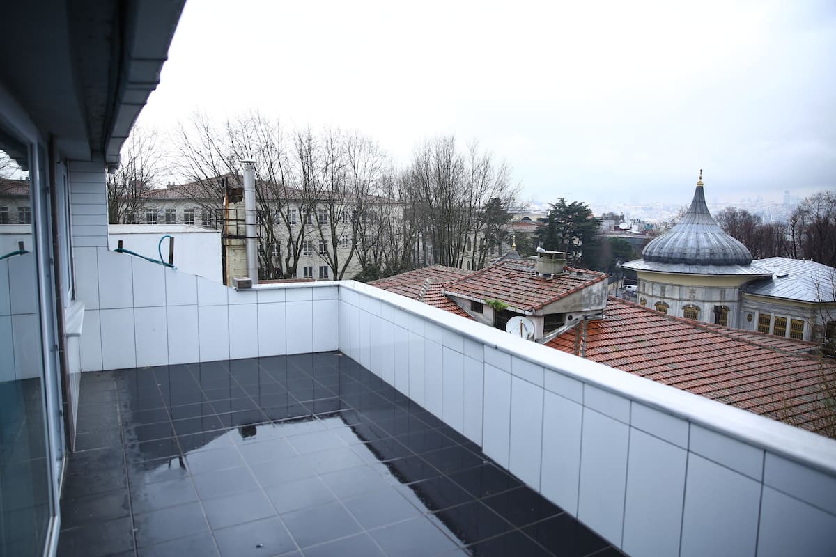 A balcony with a tiled floor, overlooking a cityscape with buildings and a dome structure.