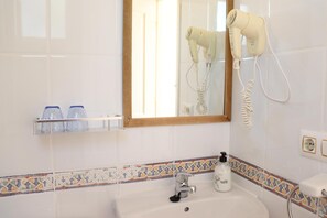 A bathroom with a sink, a mirror, a hairdryer, and a shelf with toiletries. - Hostal La Paloma I (Calpe)