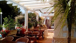 An outdoor patio with wicker furniture, potted plants, and a pergola structure. - Hostal La Paloma I (Calpe)