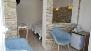 A room with a stone wall, a bed, a desk, a chair, and a small refrigerator. - Hostal La Paloma I (Calpe)