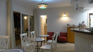 A compact kitchen with white brick walls, a small dining area with white chairs and a round table, and a red cushioned bench. - Hostal La Paloma I (Calpe)