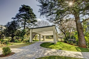 Un pavillon abrité, auquel on accède par un chemin pavé, et qui est entouré d’une végétation luxuriante et d’arbres.