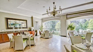 A spacious dining area with wicker furniture and a large chandelier. - The Marion on Nicol (Sandton)