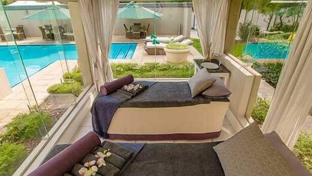 A balcony suite with a bed, seating area, and a view of a pool and garden. - The Marion on Nicol (Sandton)
