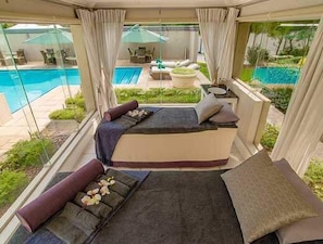 Eine Suiten-Zimmer mit Balkon, Bett, Sitzecke und Blick auf Pool und Garten.