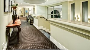 A hotel hallway with a patterned carpet, a staircase, and a large window. - The Marion on Nicol (Sandton)