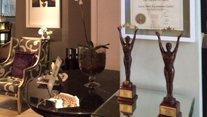 A framed award certificate for the World Luxury Hotel Awards 2014, a framed portrait, and two trophies on a glass table. - The Marion on Nicol (Sandton)