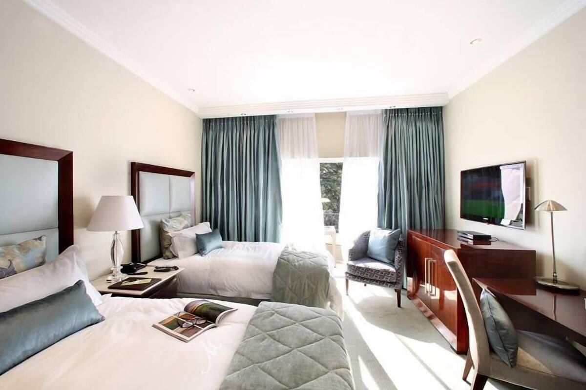 Une chambre d’hôtel avec deux lits, un bureau, une télévision et une fenêtre avec des rideaux.