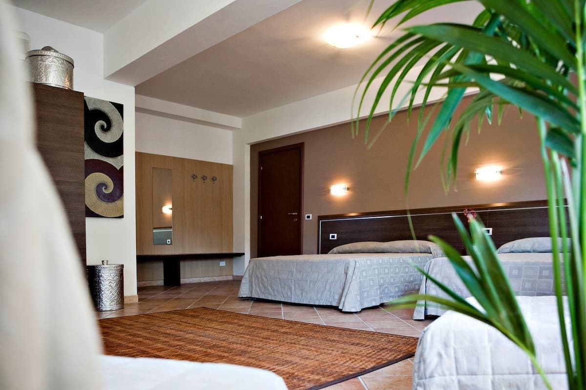 A modern hotel room with two beds, a wooden wardrobe, a large mirror, and a decorative wall piece.