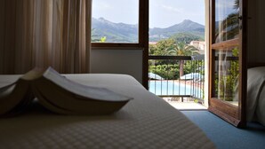 A hotel room with a bed, a book, and a view of a pool and mountains. - Hotel Marinella (Marciana Marina)
