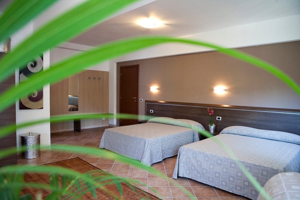 A hotel room with two beds, a wooden wardrobe, a small table, and decorative wall sconces.