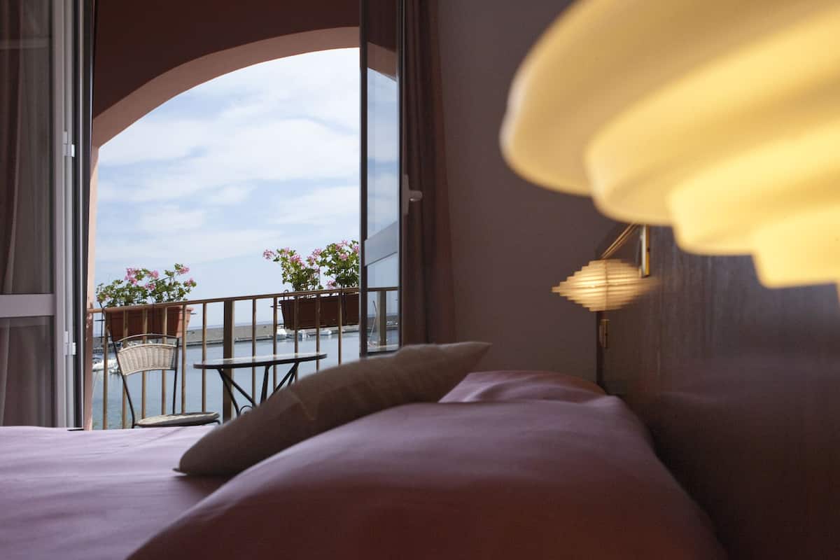 A bedroom with a view of the sea, a balcony with a table and chairs, and a lamp.