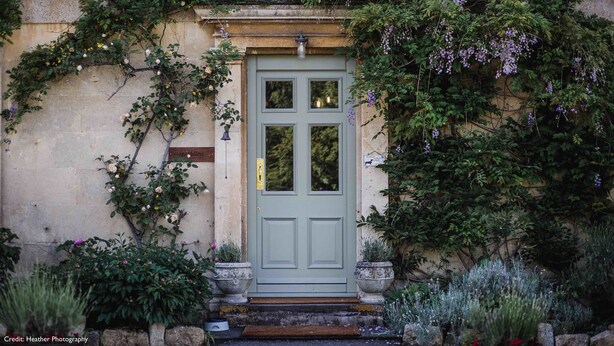 Una puerta con un porche pequeño, rodeado de follaje y flores.