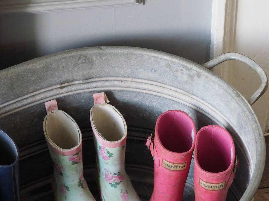 A metal bucket containing three pairs of boots, one pair with floral patterns and two pairs in pink, with a white door in the background.