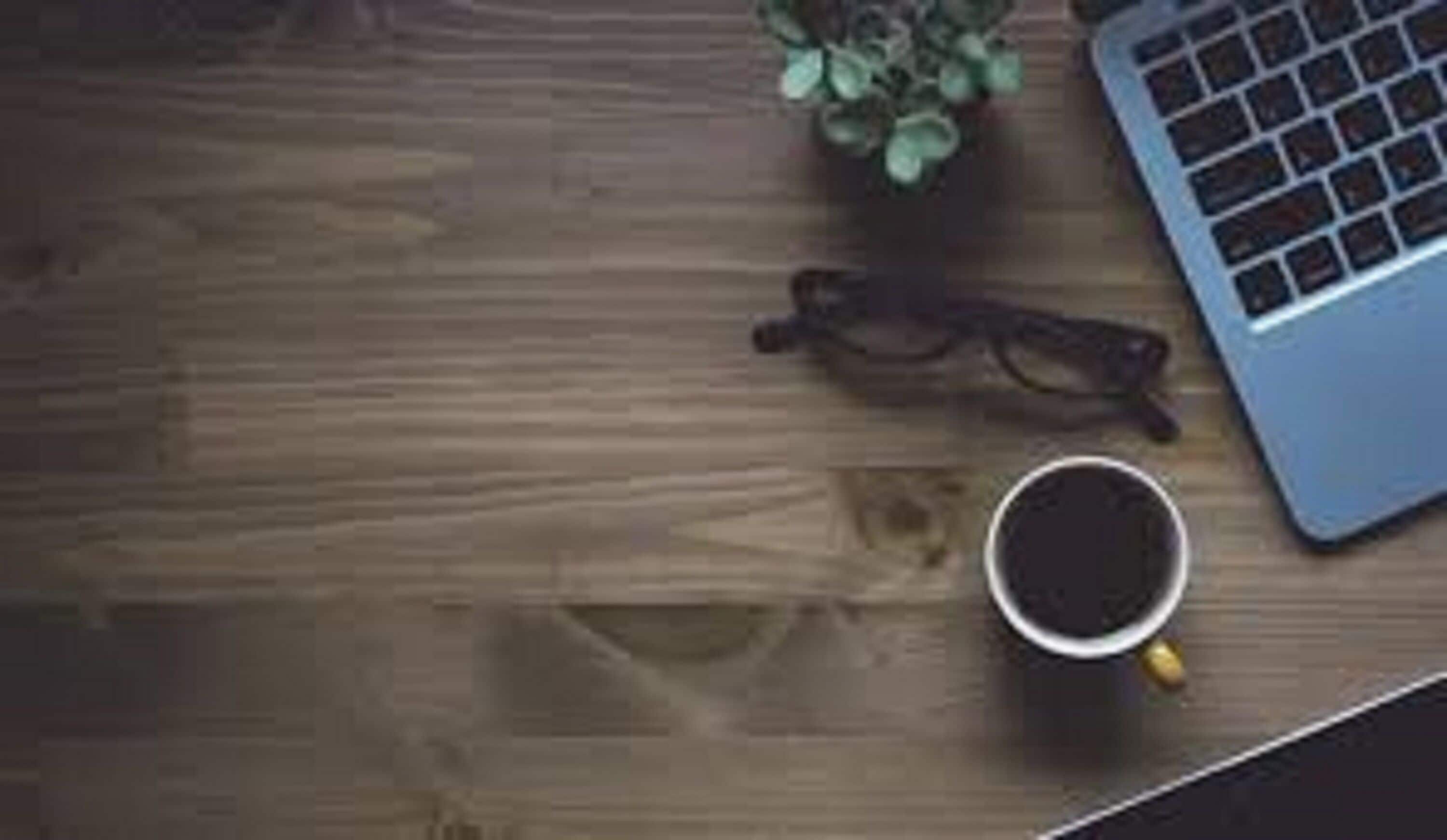 Ein Holztisch mit einem Laptop, einer Brille und einer Tasse Kaffee.
