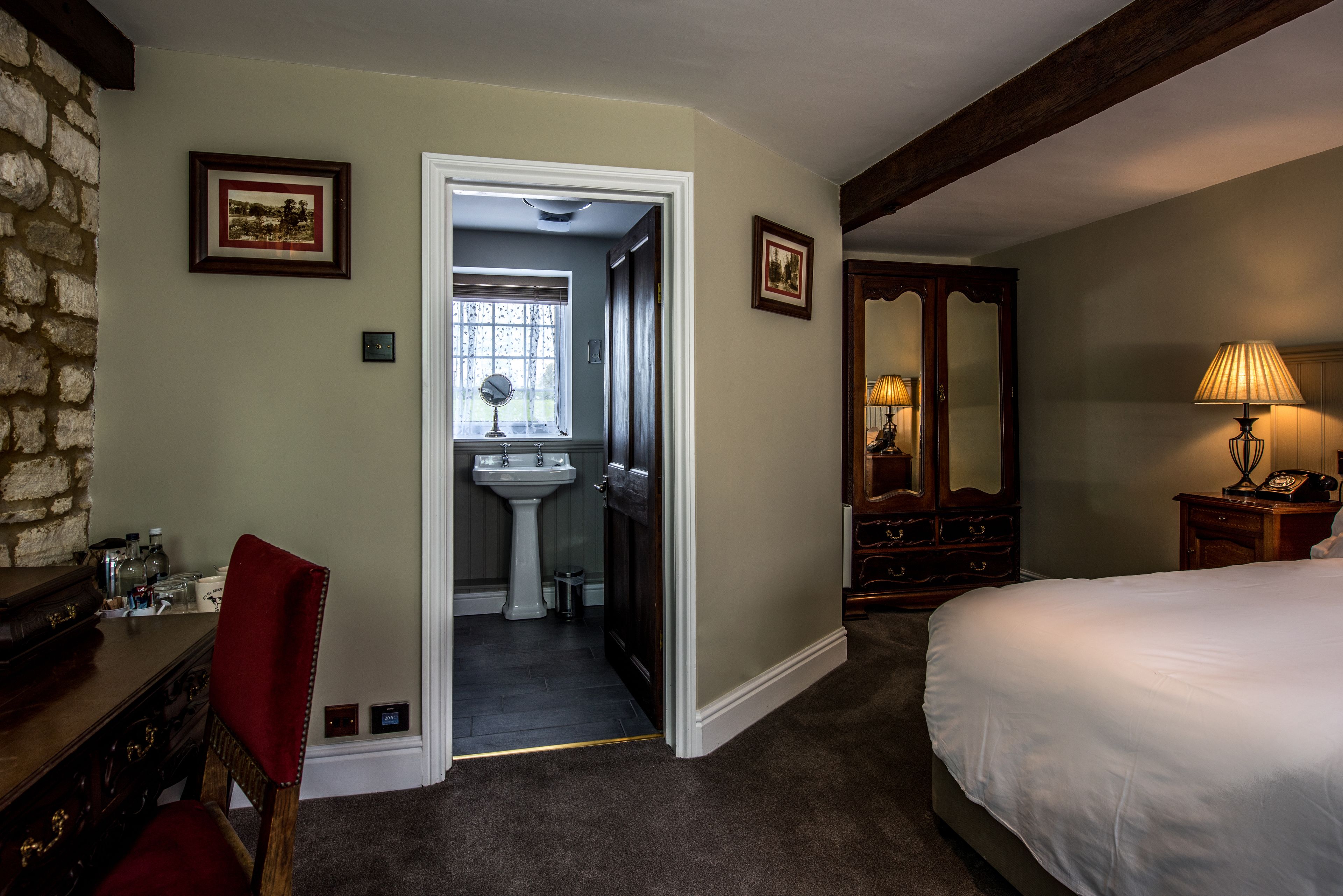 Hotelkamer met een bed, een bureau met stoel, een spiegel, een lamp en een deur naar een badkamer.