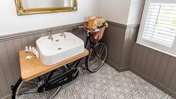 Een badkamer met een witte wastafel, een houten aanrecht en een fiets met mand op de vloer.