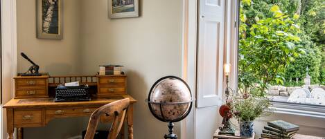 A study room with a wooden desk, a globe, and a window with a view of greenery.
