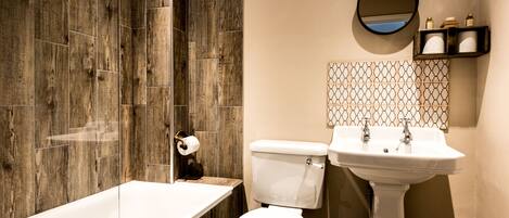A bathroom with a wooden shower wall, a white toilet, a sink, and a mirror.