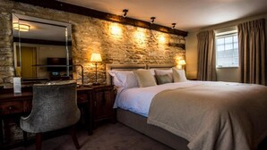 Un dormitorio con pared de piedra, una cama con ropa blanca, un escritorio con silla y dos lámparas de noche.