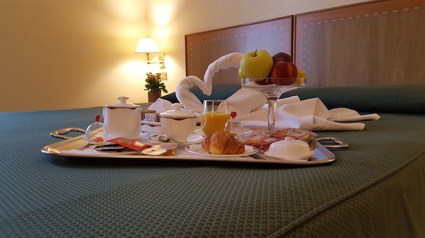A breakfast tray with croissants, a glass of orange juice, a teapot, and a fruit bowl on a bed.