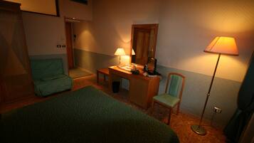 A hotel room with a bed, a desk with a lamp, a chair, and a standing lamp.
