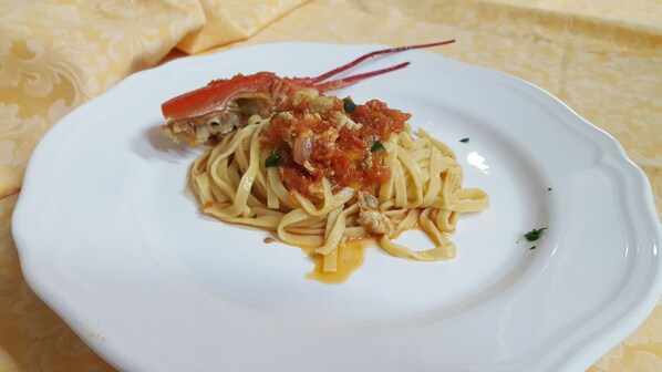 A plate of spaghetti with a tomato-based sauce and a piece of crab meat on a white plate. - Nuovo Albergo (Chieti)