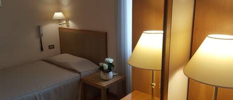 A hotel room with a single bed, bedside table, lamp, and a mirror.