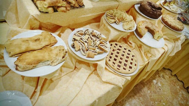Una mesa de bufé con diversas opciones de repostería, incluyendo croissants, tartas y pasteles.