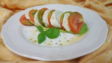 A white plate with a layered salad consisting of tomatoes, mozzarella, and basil leaves, garnished with olive oil and herbs.