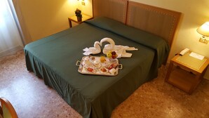 Una cama bien hecha con una colcha verde, una bandeja con alimentos para el desayuno y adornos con forma de cisnes en la cama.