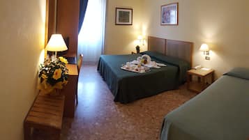 Ein Hotelzimmer mit einem Bett, einem Nachttisch, einer Lampe, einem kleinen Tisch mit Blumenvase und einem an der Wand befestigten Telefon.