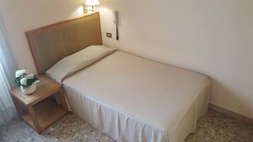 Una cama individual con cabecera de madera, una mesita de noche con lámpara y un teléfono en la pared.