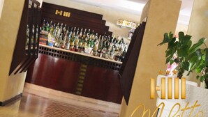 A bar area with a variety of liquor bottles, a wooden counter, and a potted plant. - Hotel Miletto (San Massimo)