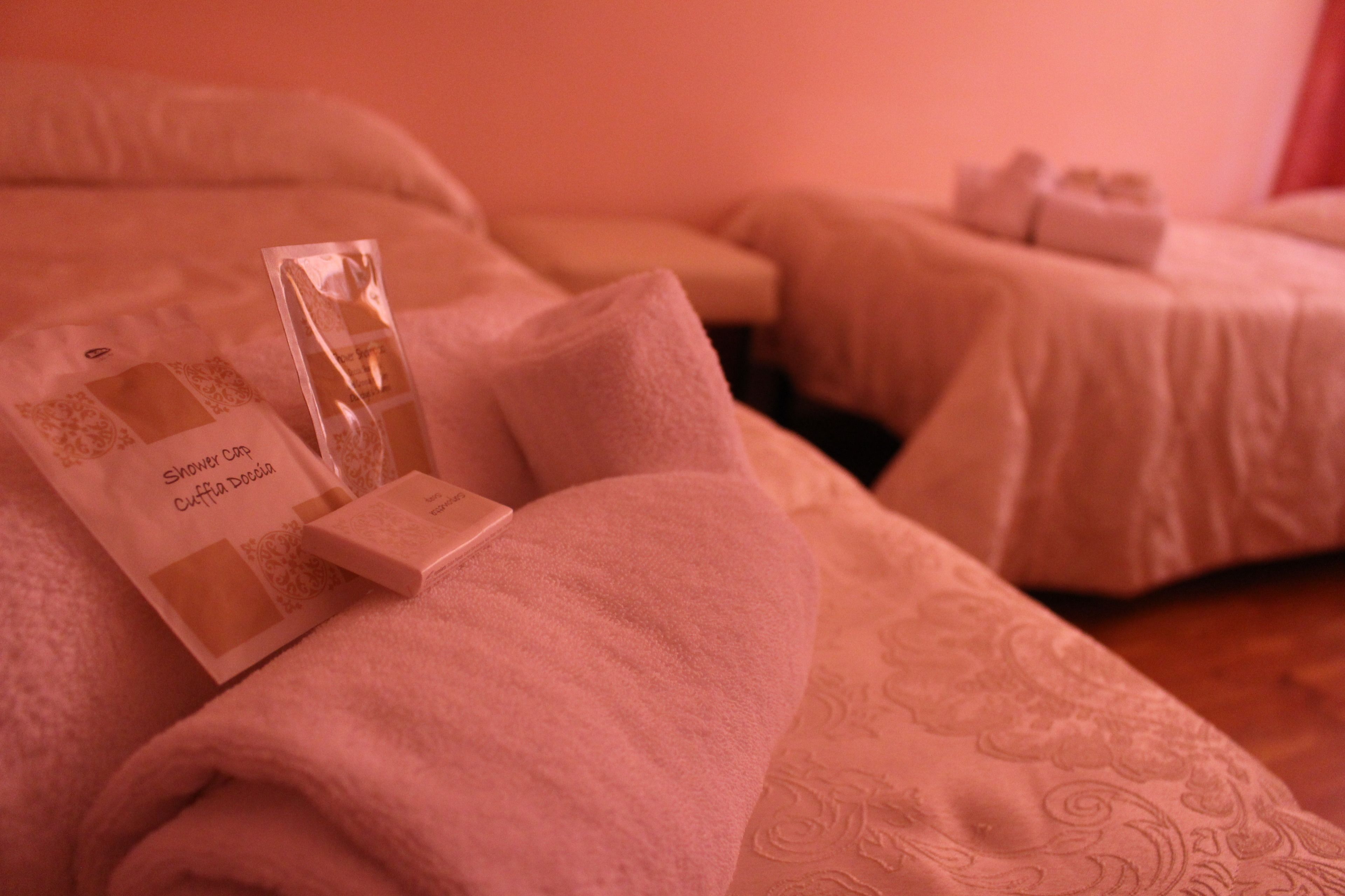 Une chambre d’hôtel avec deux lits, chacun recouvert d’une serviette rose et d’un oreiller blanc. On trouve des articles de toilette sur les lits, notamment une bouteille et une boîte.