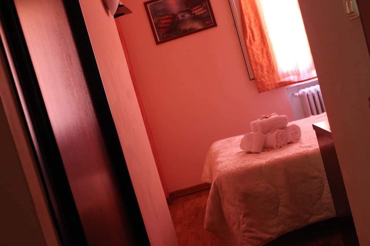 A hotel room with a bed, a window with curtains, and a painting on the wall.