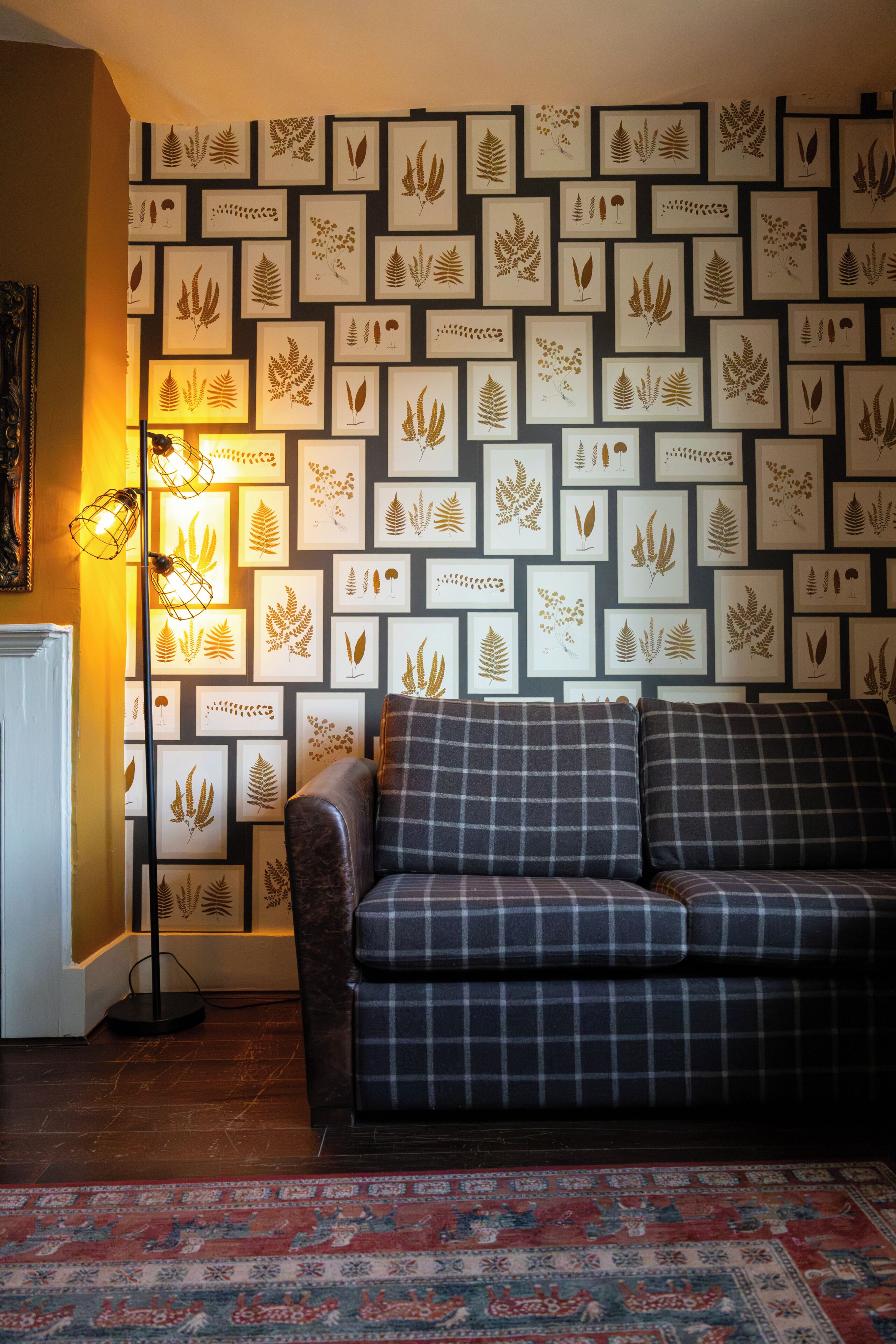 A room with a patterned wall, a sofa, a floor lamp, and a patterned rug.