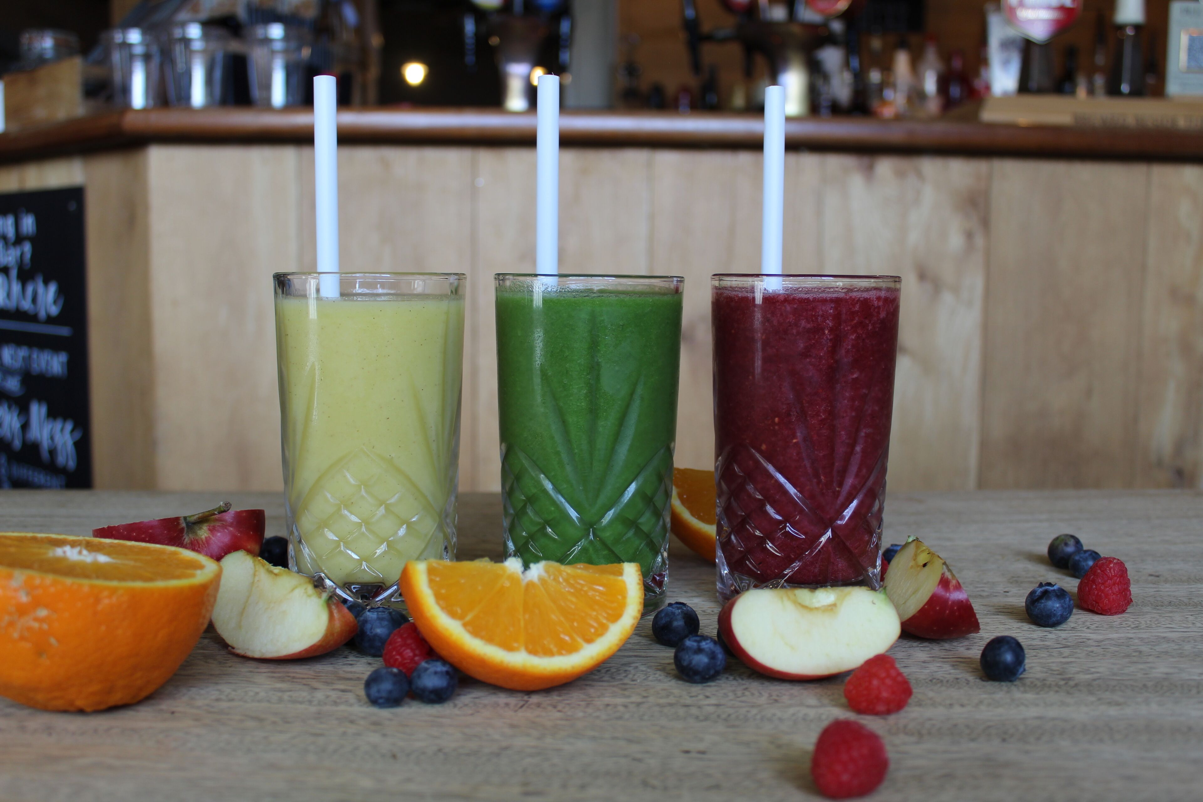 Three glasses of smoothies with straws, surrounded by fruit slices on a wooden surface.