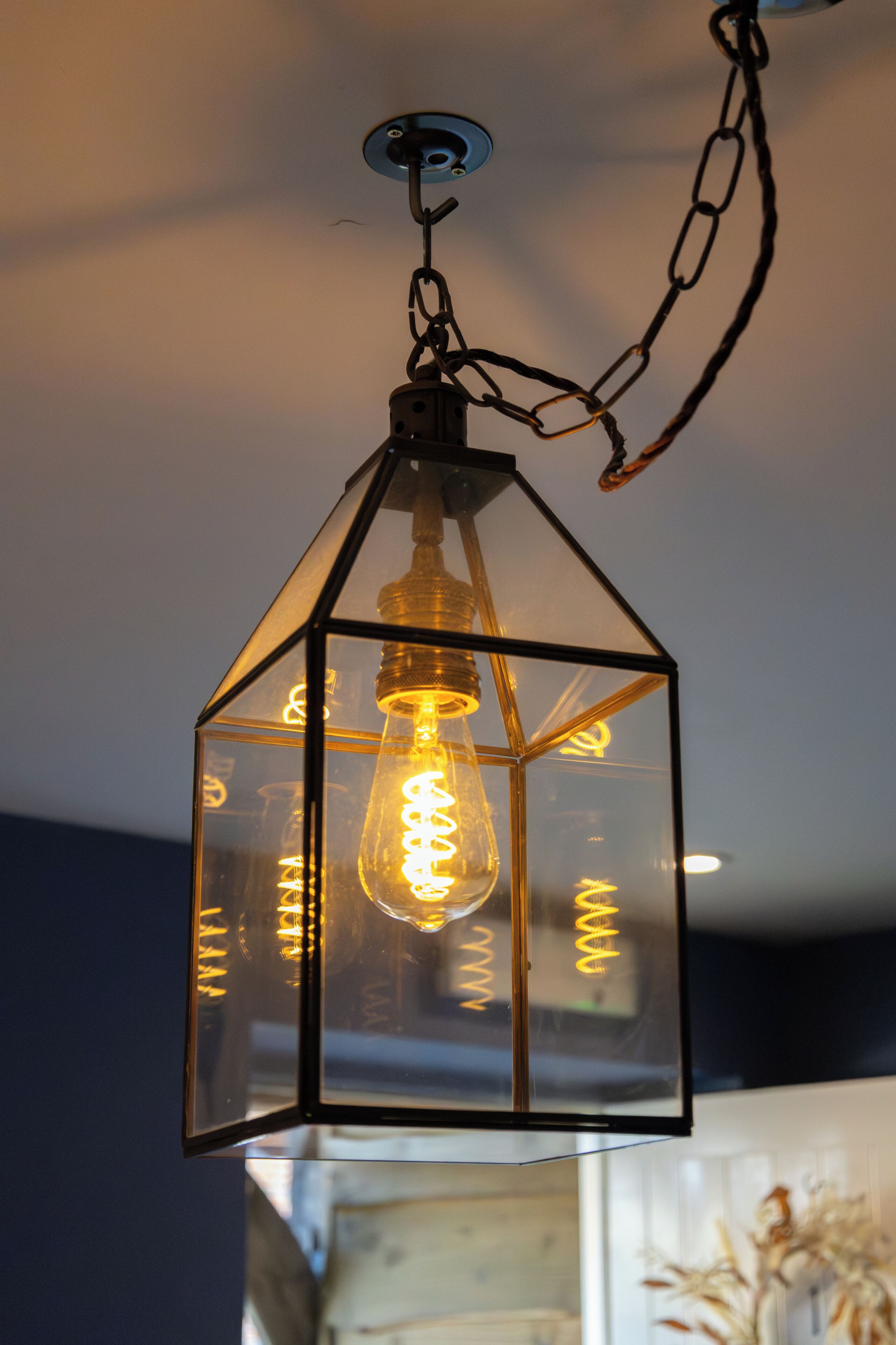Una lámpara colgante con pantalla de vidrio transparente y bombilla de filamento visible.