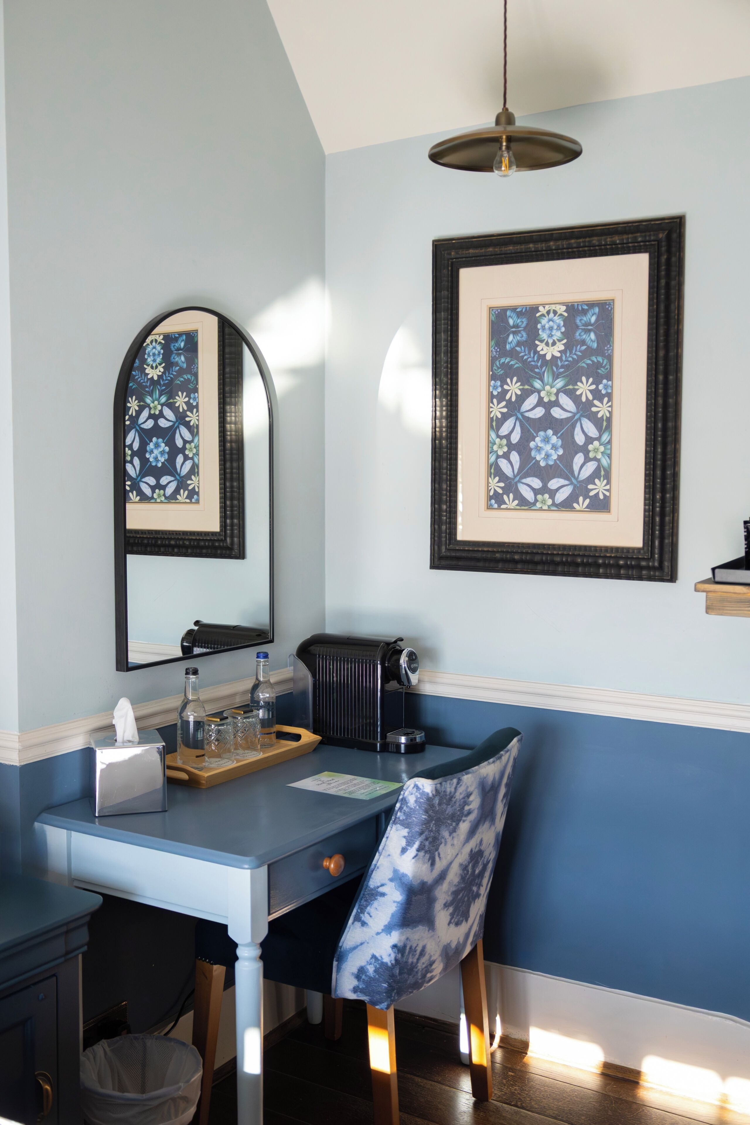 A room with a desk, chair, mirror, framed artwork, and a radiator.