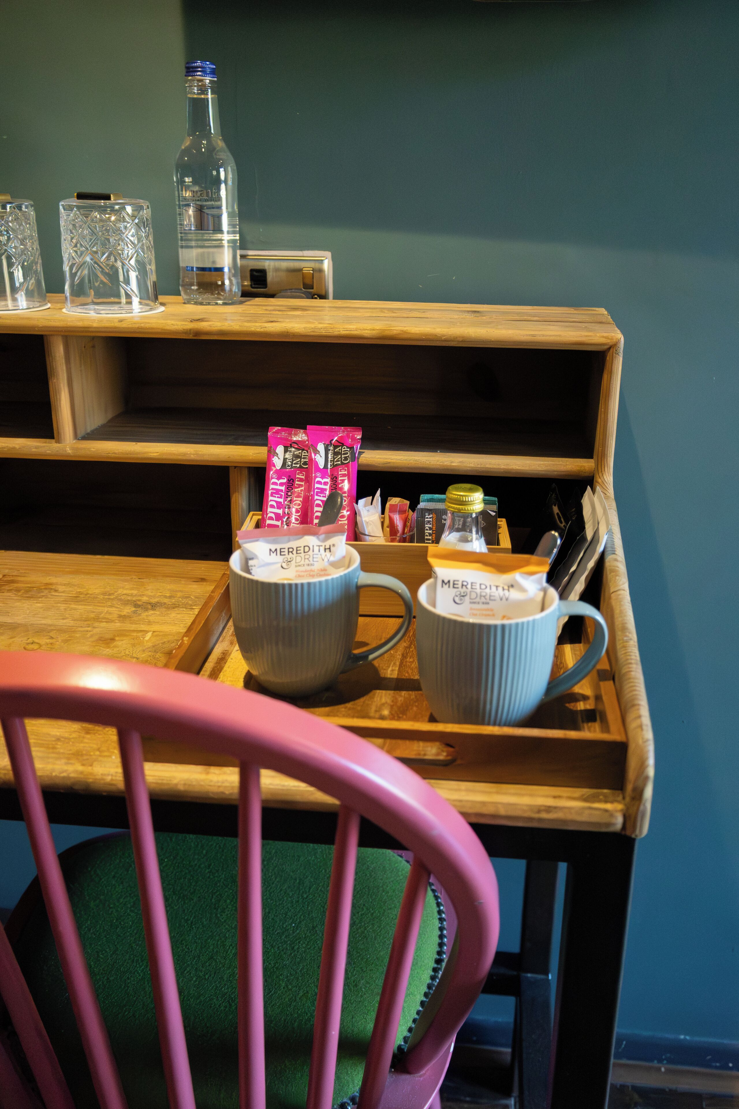 A wooden table with two mugs, a bottle, and some snacks.