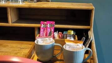 A wooden table with two mugs, a bottle, and some snacks.