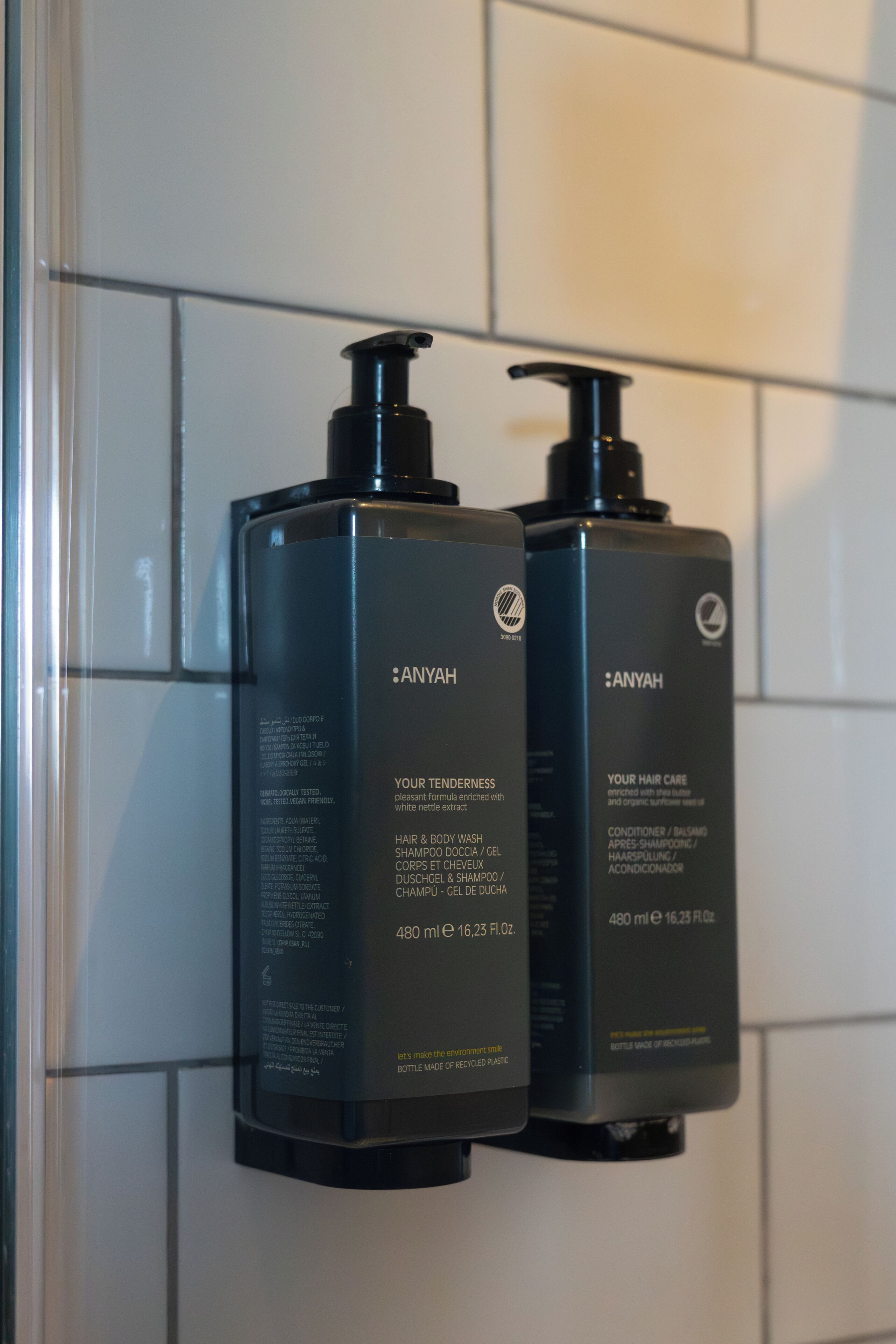 Two black bottles of Anyah hair care products mounted on a wall.