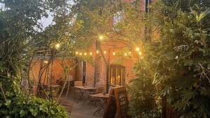 En murstensbygning med en havepatio, udendørs møbler og lyskæder.