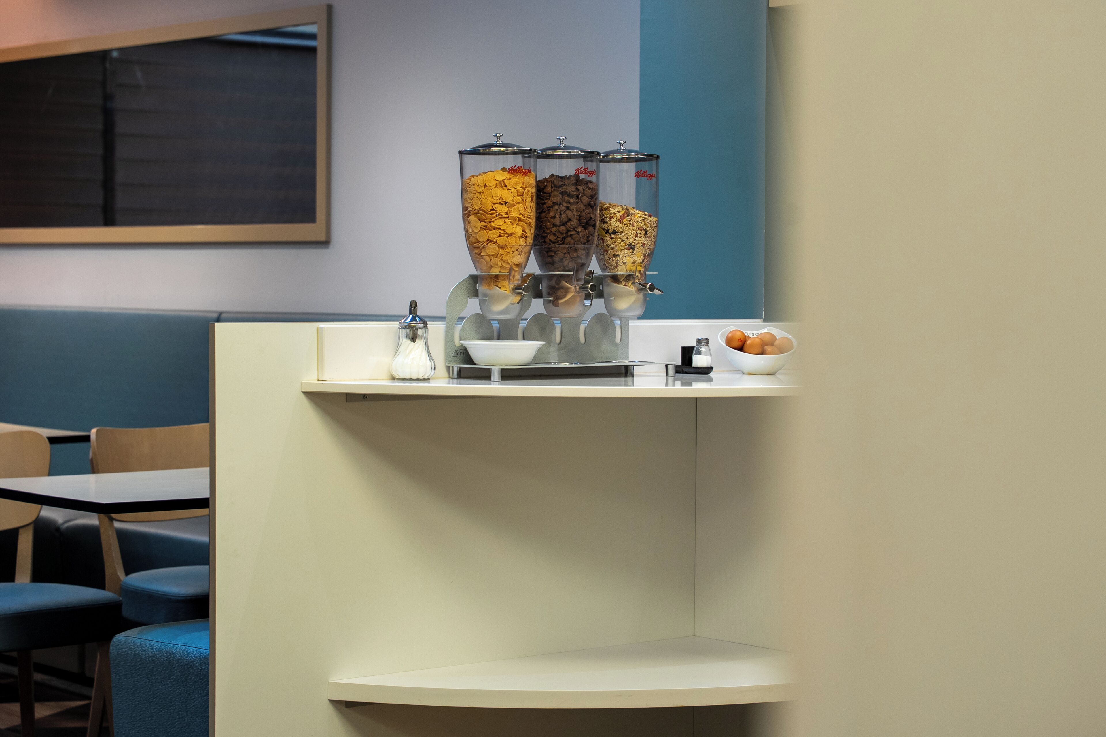 A breakfast bar with a cereal dispenser, a bowl, and a small plate with a pastry.