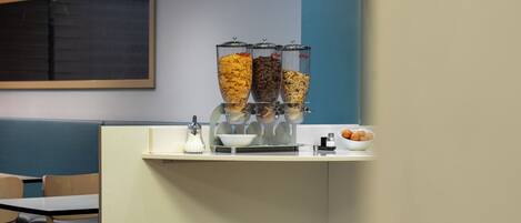 A breakfast bar with a cereal dispenser, a bowl, and a small plate with a pastry.