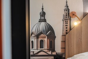 Une chambre avec une grande fresque murale représentant un bâtiment historique, une tête de lit en bois et une lampe de chevet.