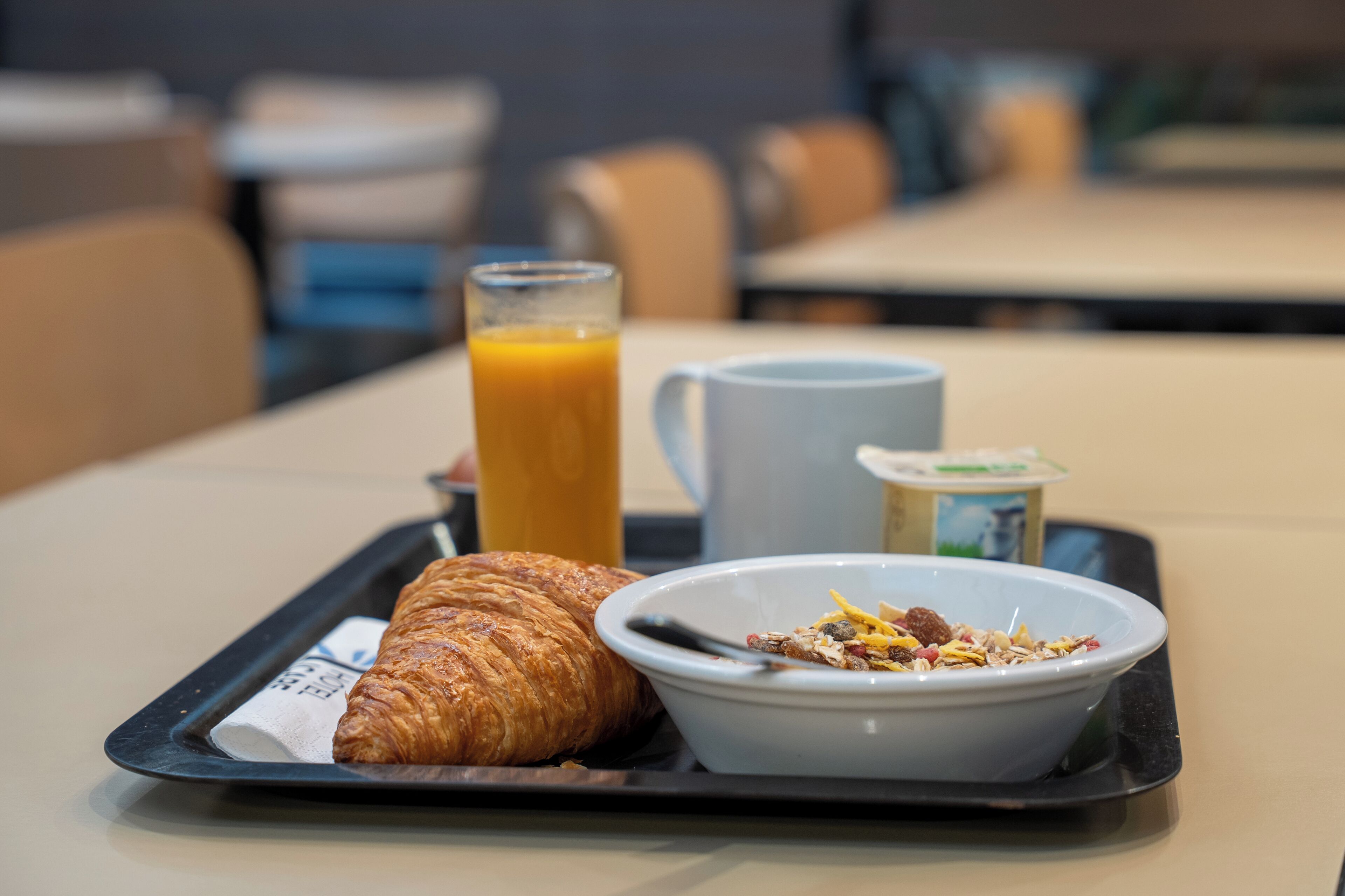 Ein Frühstücksbrett mit einem Croissant, einem Glas Orangensaft, einer Tasse und einer Schüssel Müsli mit Früchten und Nüssen.
